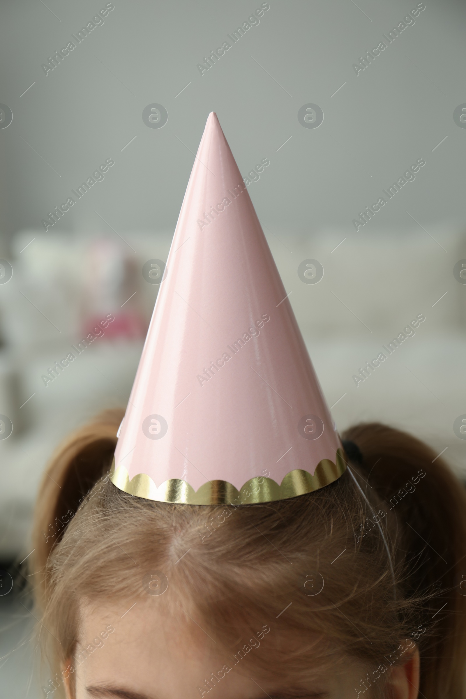 Photo of Little girl wearing party hat at home, closeup