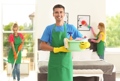 Photo of Team of professional janitors in uniform cleaning bedroom