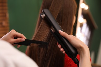 Photo of Stylist straightening woman's hair with flat iron in salon