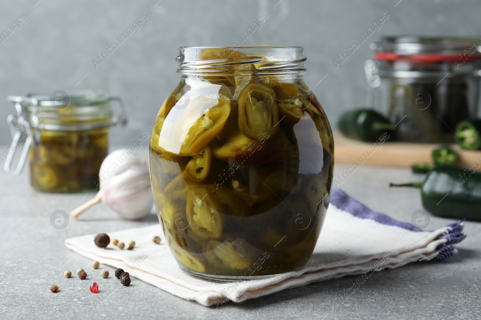 Photo of Glass jar with slices of pickled green jalapeno peppers on light grey table