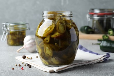 Glass jar with slices of pickled green jalapeno peppers on light grey table