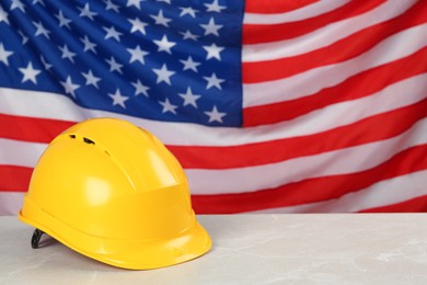 Photo of Yellow protective hard hat on light grey table against American flag. Space for text