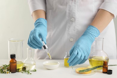 Scientist developing cosmetic oil at white table, closeup