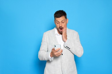 Photo of Emotional man looking at smartphone on light blue background. Space for text