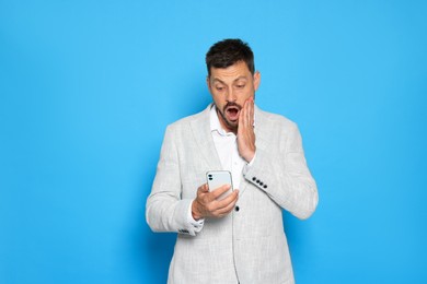 Emotional man looking at smartphone on light blue background. Space for text