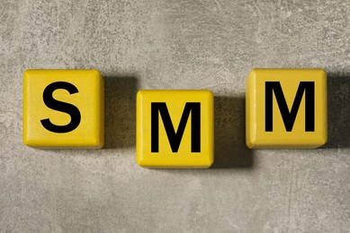 Photo of Yellow cubes with letters SMM on grey stone background, flat lay