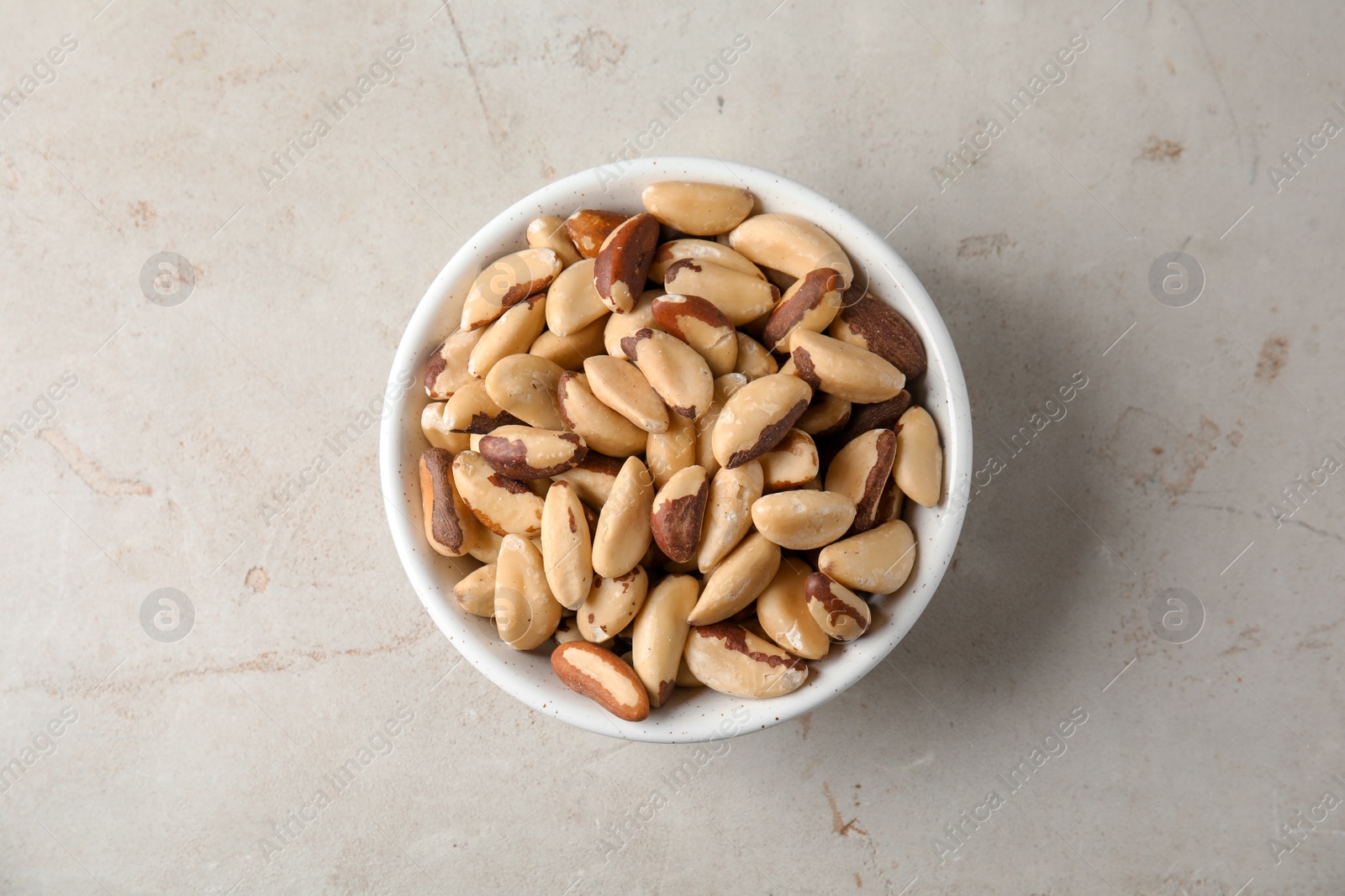 Photo of Bowl with tasty Brazil nuts on grey background, top view