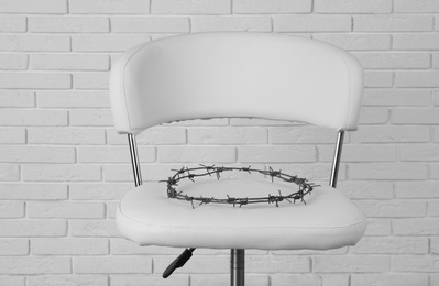 Photo of Chair with barbed wire near white brick wall. Hemorrhoids concept