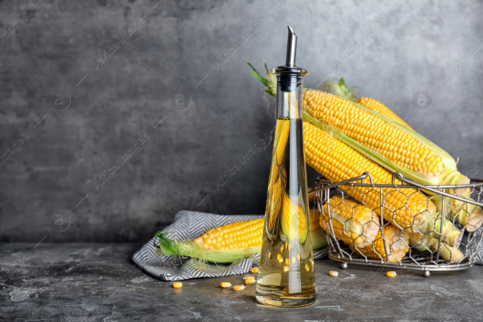 Photo of Bottle of corn oil and fresh cobs on table against dark wall