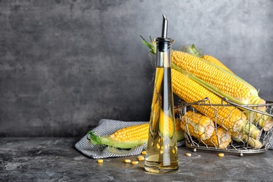 Bottle of corn oil and fresh cobs on table against dark wall