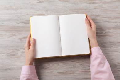 Photo of Woman holding open notebook at white wooden table, top view