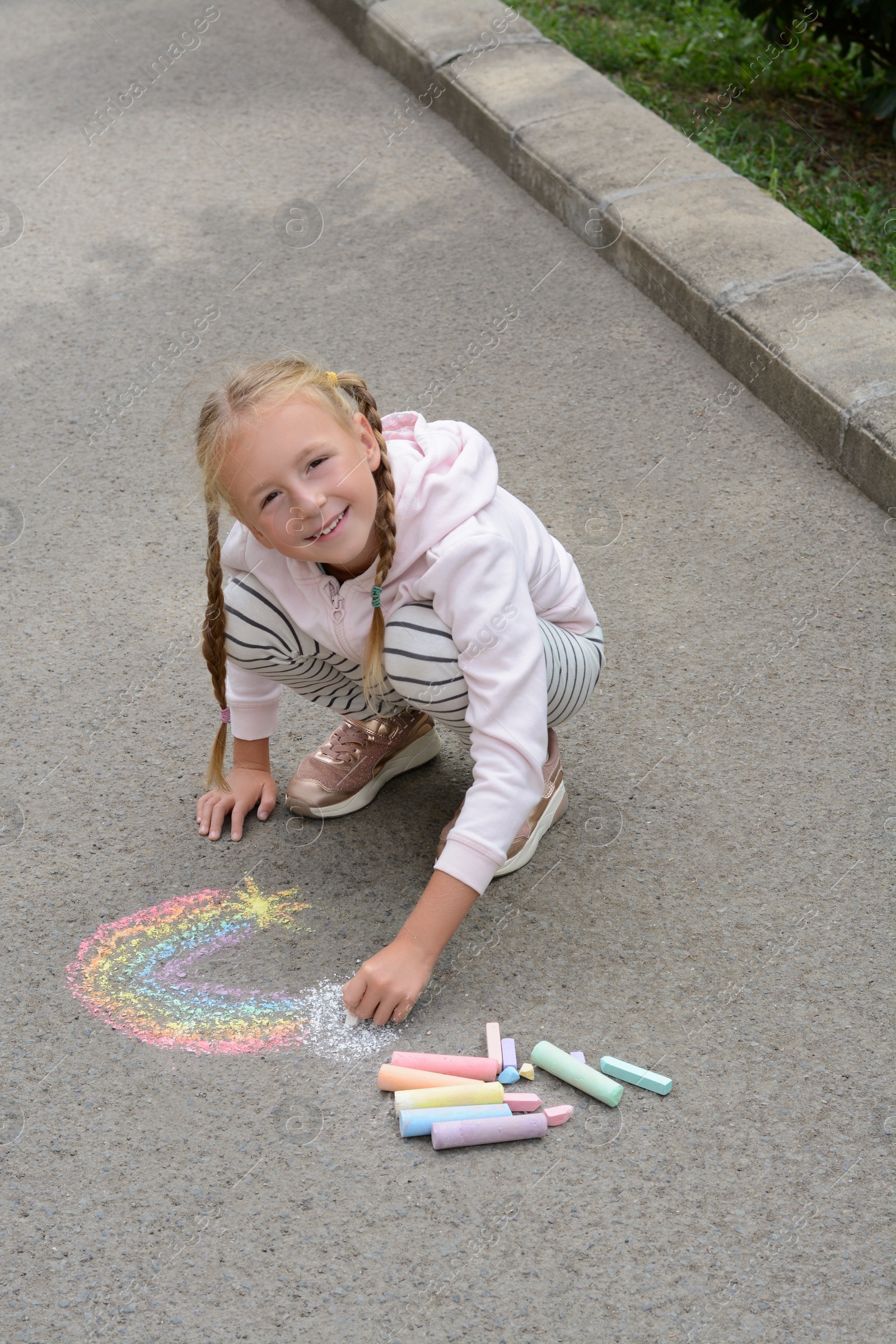 Photo of Little child drawing rainbow with chalk on asphalt