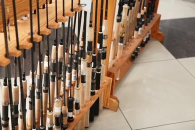 Photo of Stand with different fishing rods in sports shop, closeup