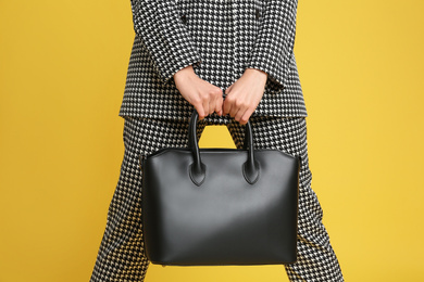 Young woman with stylish bag on yellow background, closeup