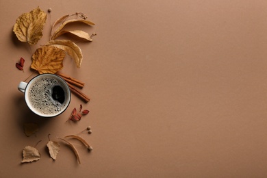 Photo of Flat lay composition with cup of hot drink and autumn leaves on brown background, space for text. Cozy atmosphere
