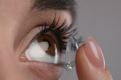 Photo of Closeup view of young woman putting contact lens in her eye against grey background