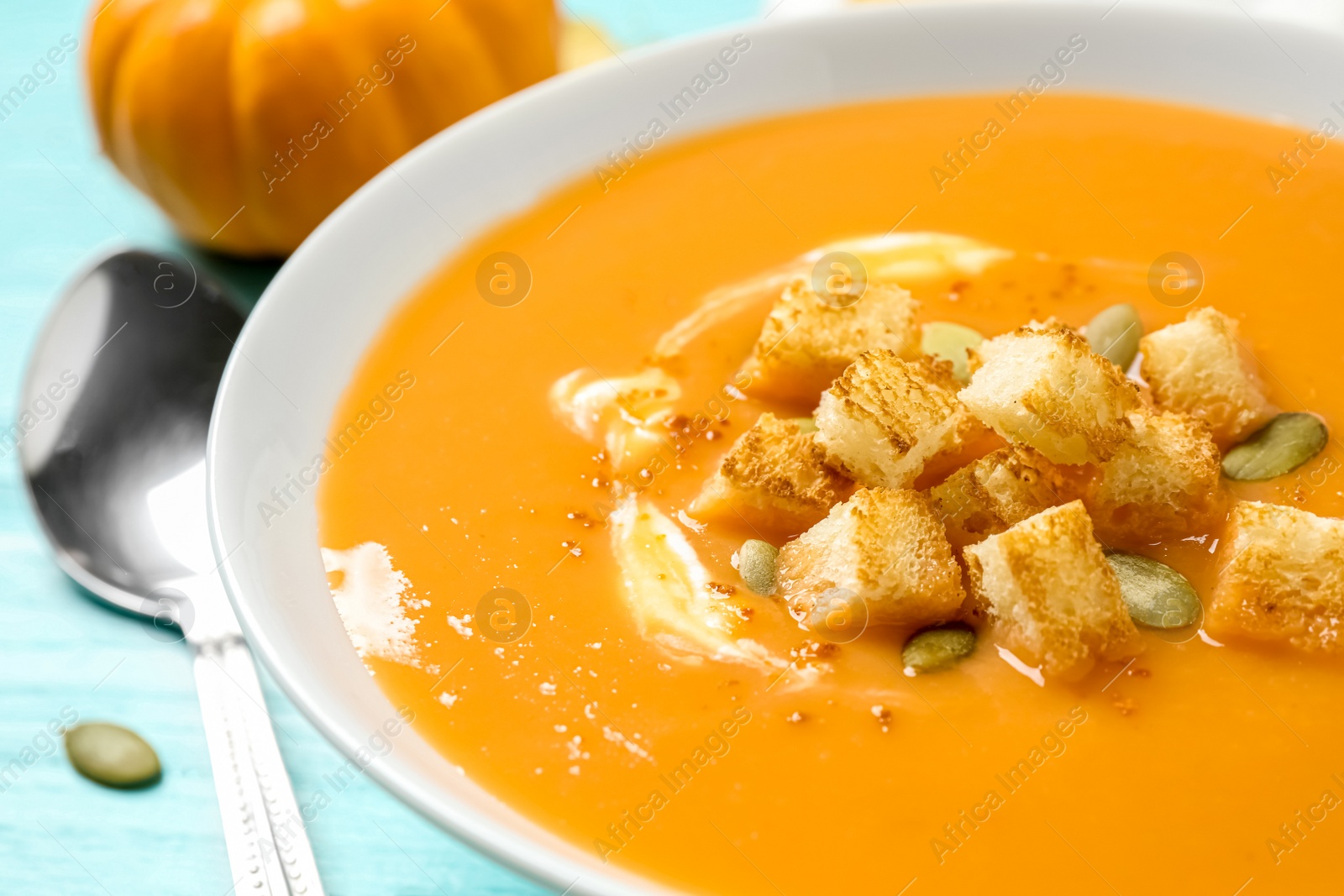 Photo of Tasty creamy pumpkin soup with croutons and seeds in bowl on table, closeup