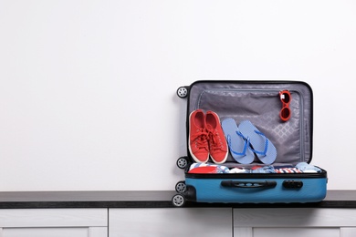 Photo of Packed suitcase with clothes and shoes on chest of drawers indoors. Space for text