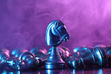 Photo of Metal knight among fallen chess pieces on checkerboard in color light, closeup