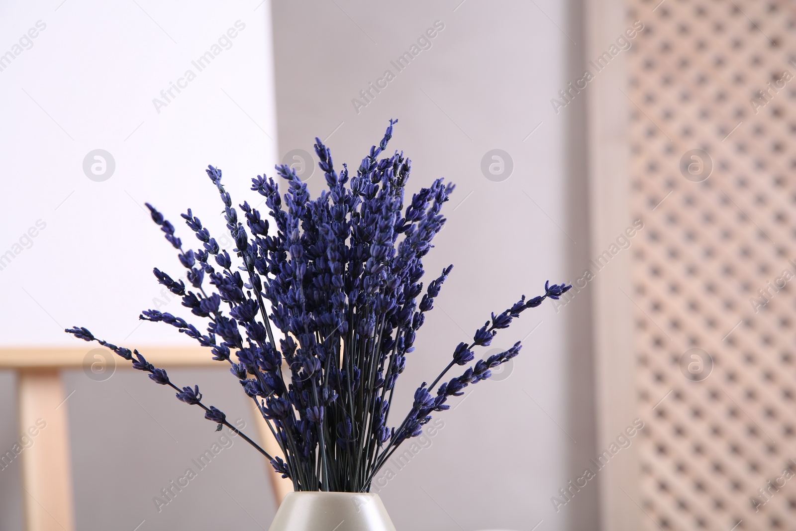 Photo of Bouquet of beautiful preserved lavender flowers near easel indoors, closeup. Space for text