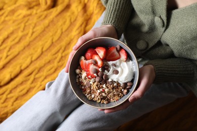 Photo of Woman holding bowl of tasty granola with chocolate chips, strawberries and yogurt indoors, top view