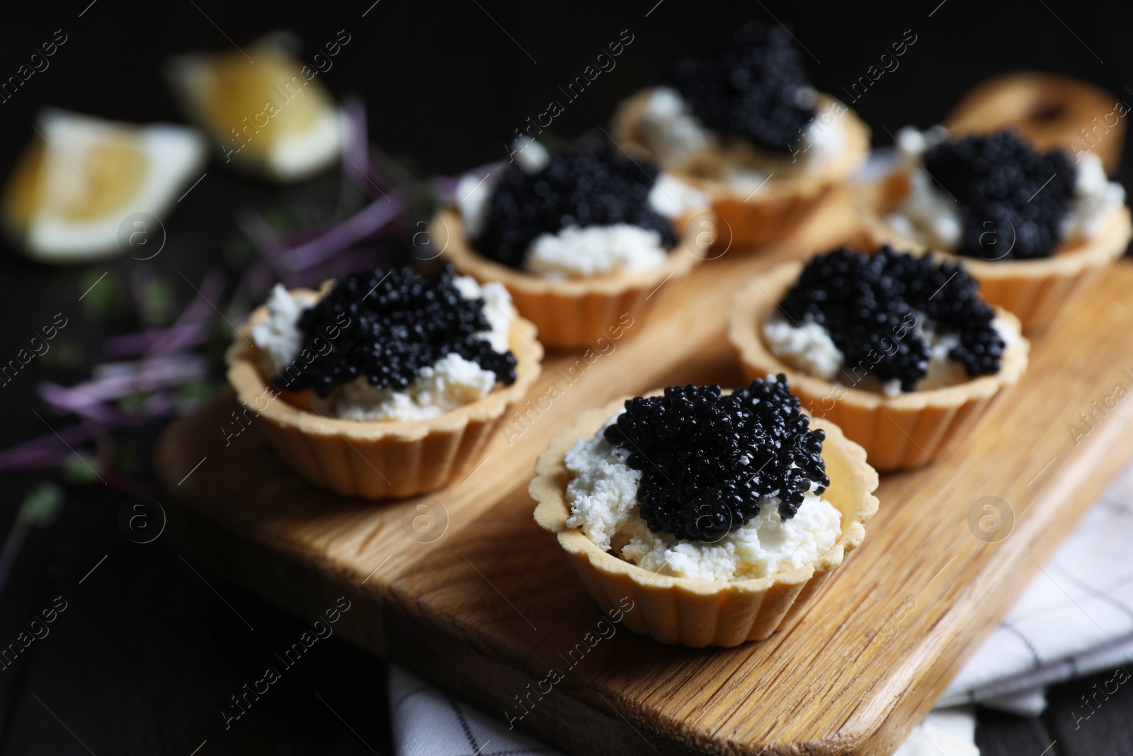 Photo of Board of delicious tartlets with black caviar and cream cheese on wooden table, closeup