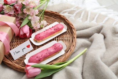 Photo of Tasty breakfast served in bed. Delicious eclairs, tea, flowers, gift box and card with phrase I Love You on blanket