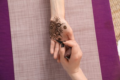 Photo of Professional mehndi master making henna tattoo at table, top view