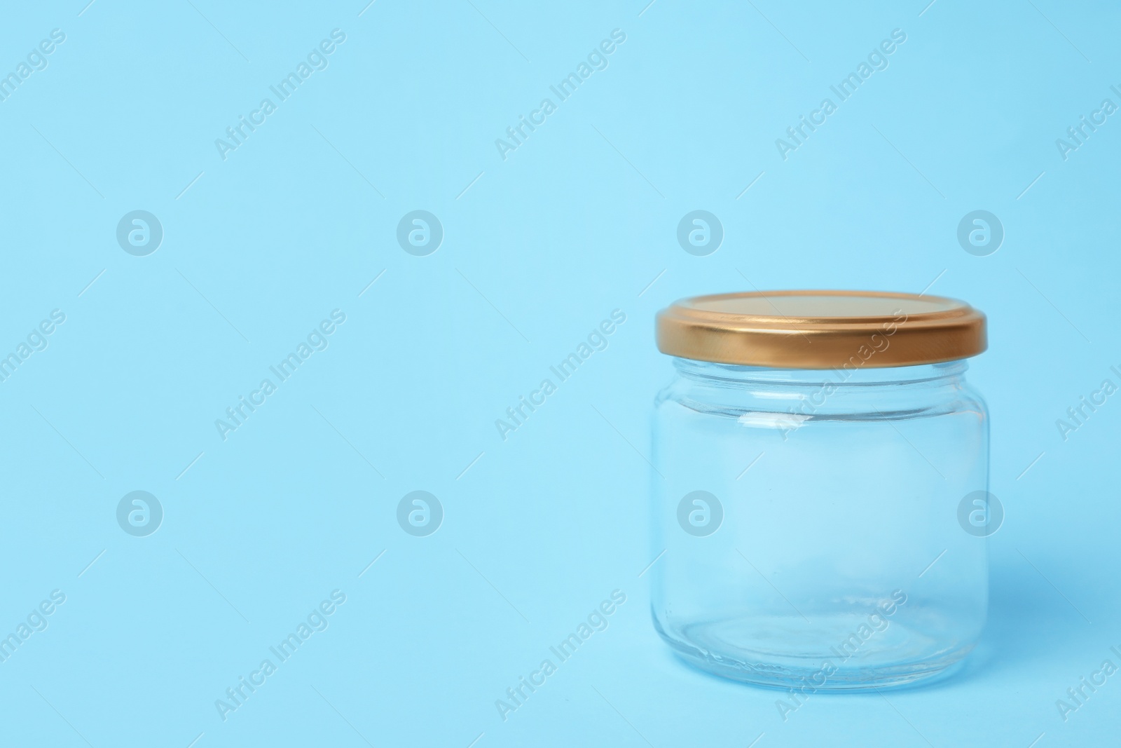 Photo of Closed empty glass jar on light blue background, space for text