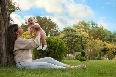 Photo of Happy mother with adorable baby sitting on green grass in park