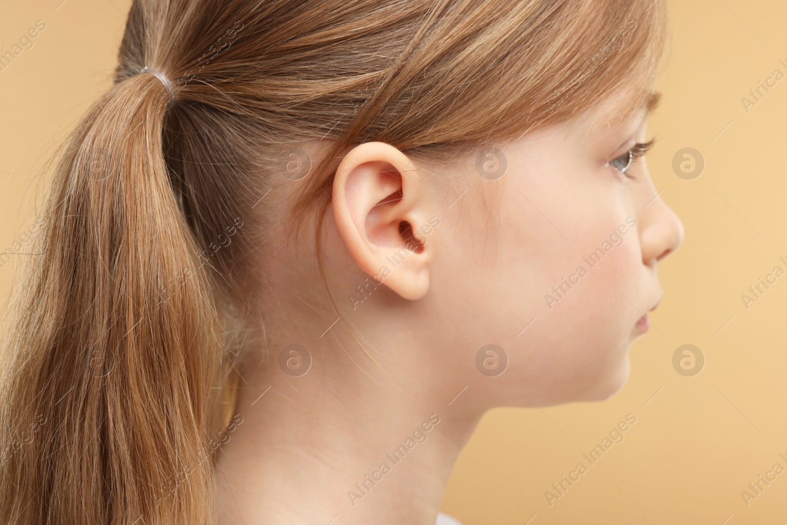 Photo of Hearing problem. Little girl on pale brown background, closeup of ear