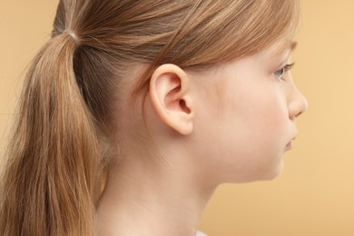 Hearing problem. Little girl on pale brown background, closeup of ear