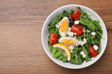 Delicious salad with boiled egg, tomatoes and cheese in bowl on wooden table, top view. Space for text