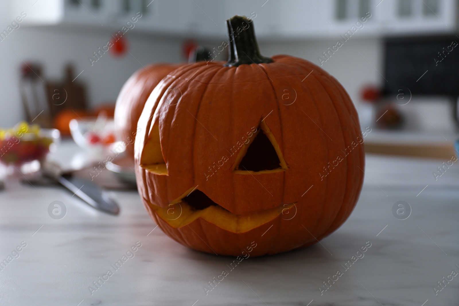 Photo of Pumpkin jack o'lantern on white marble table in kitchen. Halloween celebration