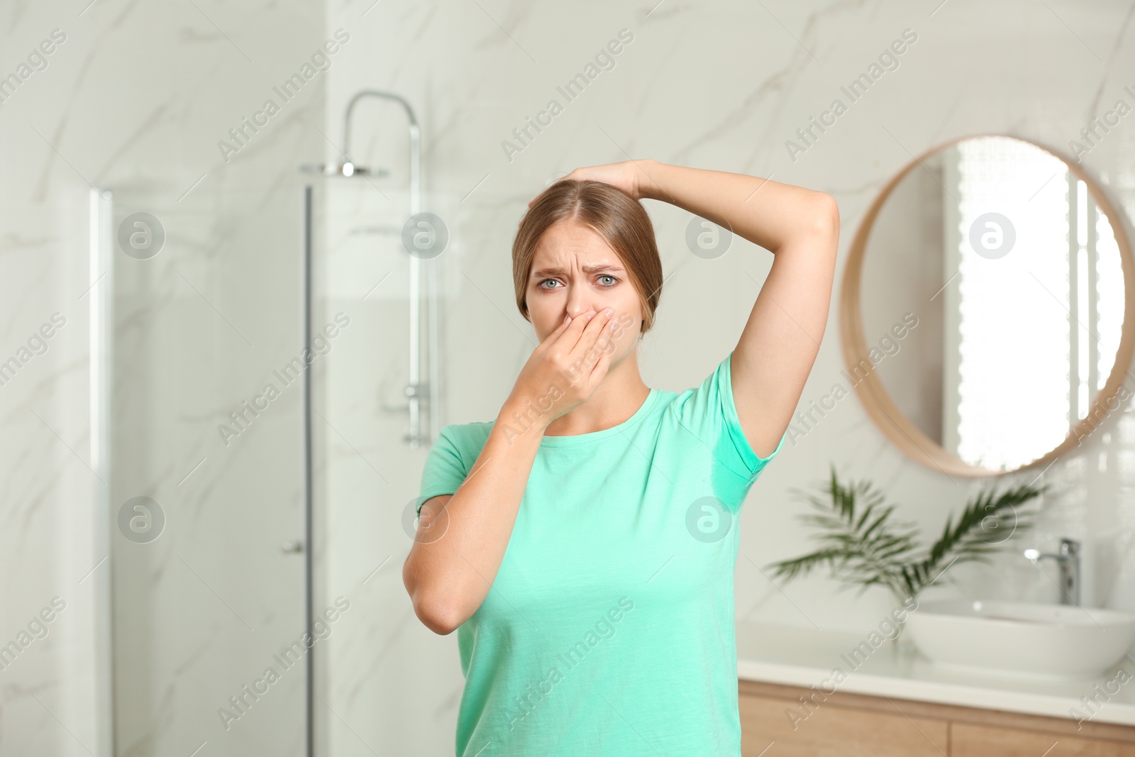 Photo of Young woman with sweat stain on her clothes in bathroom. Using deodorant