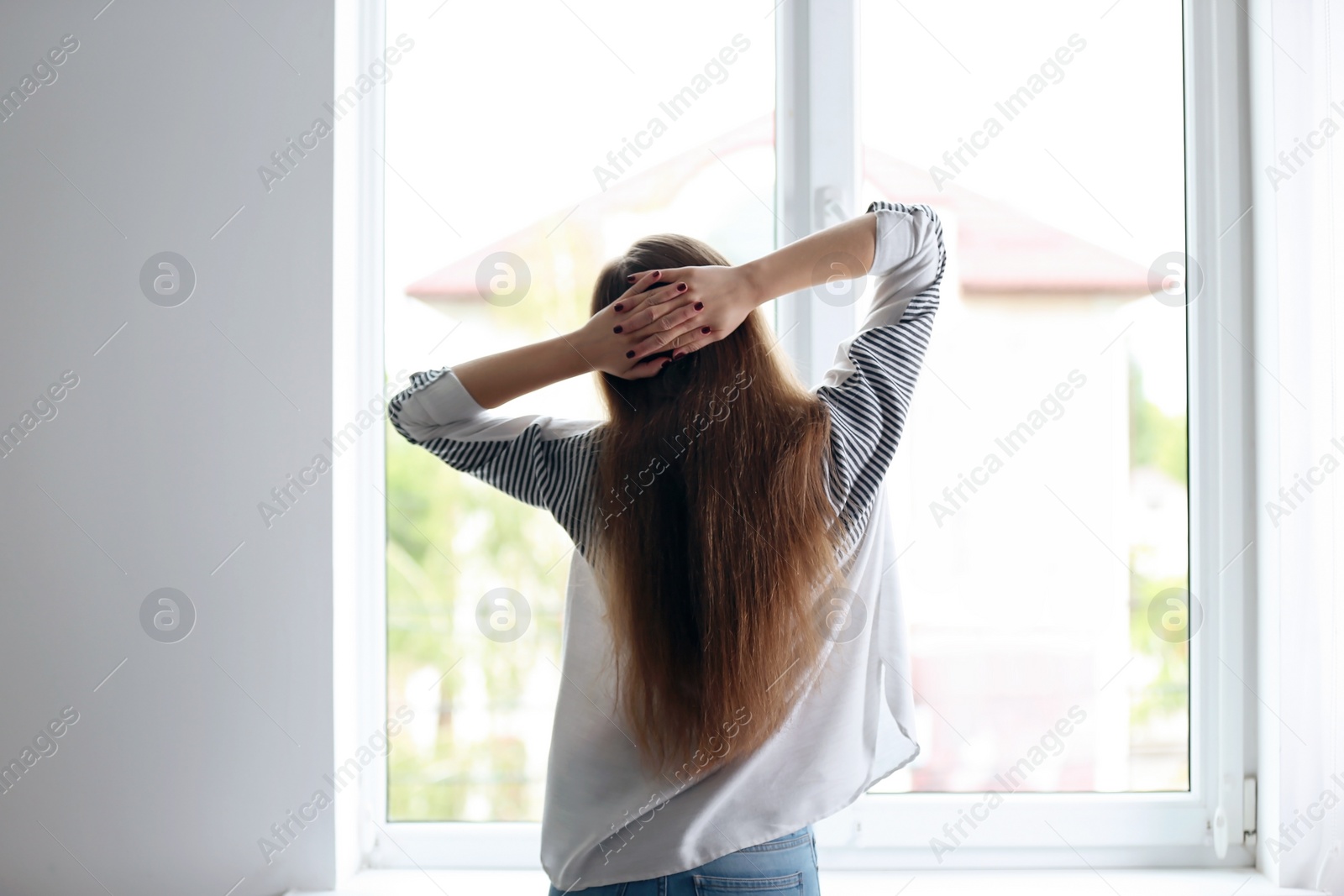 Photo of Young beautiful woman standing near window at home