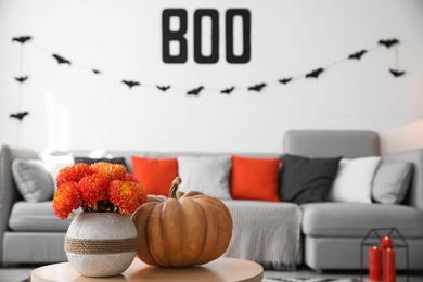 Photo of Modern room decorated for Halloween, focus on table with pumpkin and flowers. Festive interior