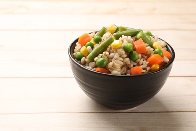 Delicious pearl barley with vegetables in bowl on wooden table, closeup. Space for text