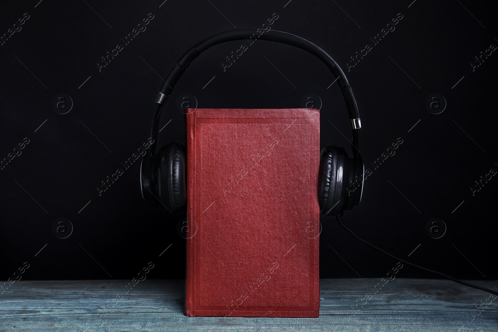 Photo of Book and modern headphones on wooden table against black background