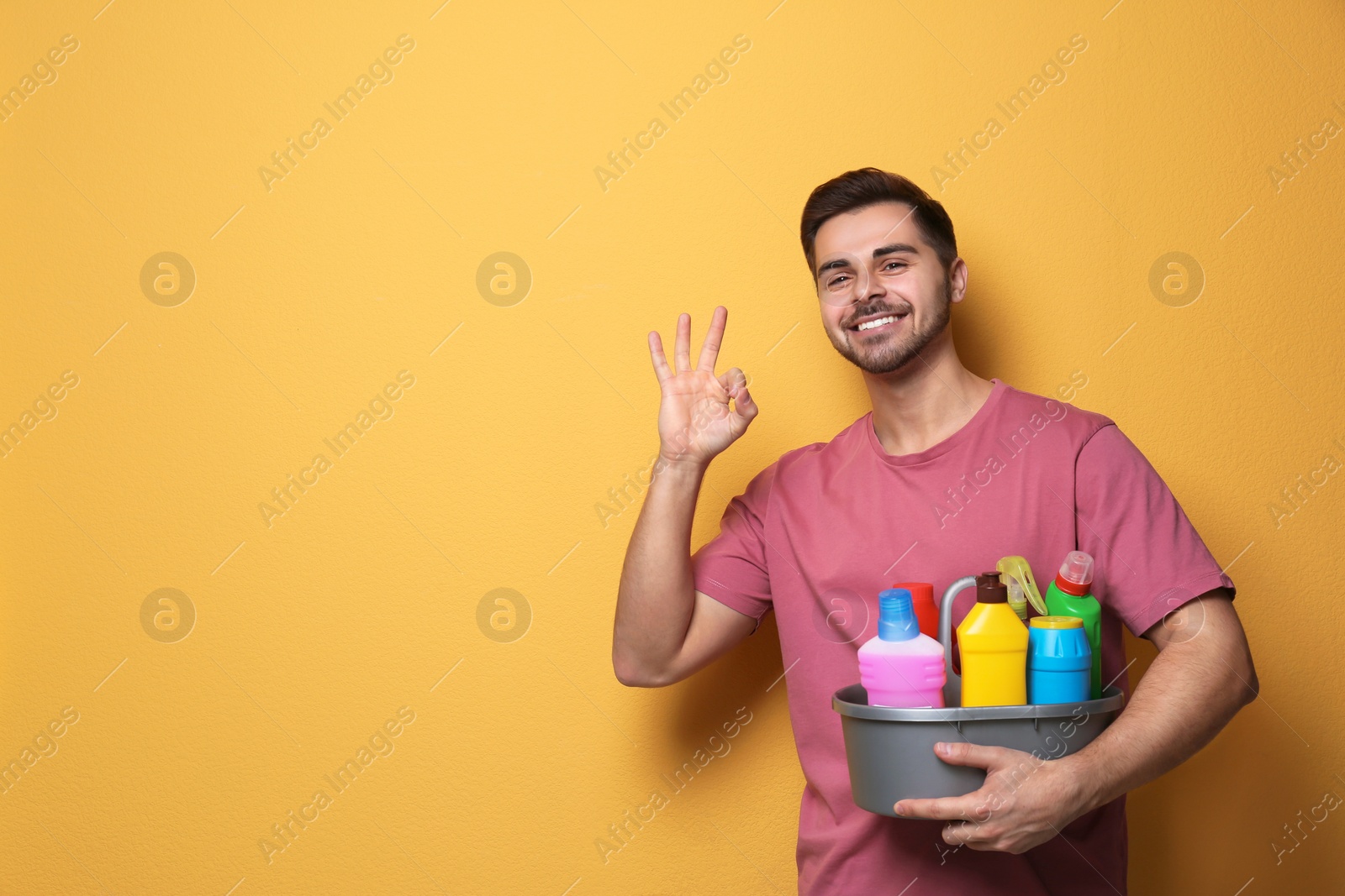 Photo of Man with basin of detergents on color background. Space for text