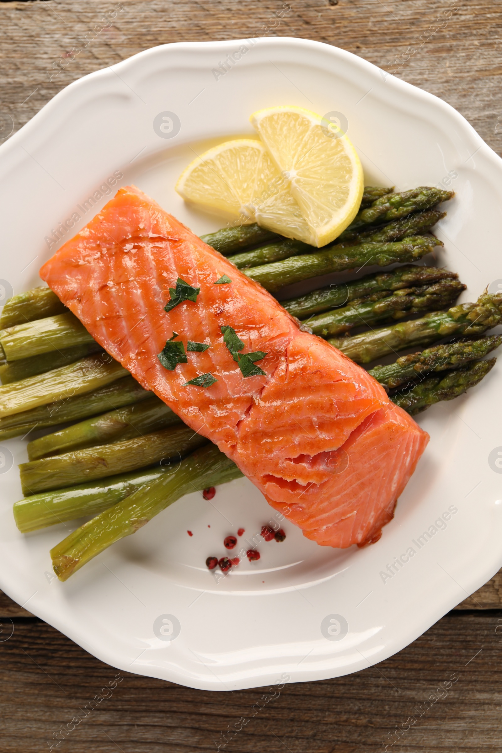 Photo of Tasty grilled salmon with asparagus and lemon on wooden table, top view