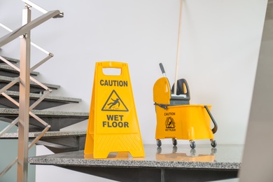 Safety sign with phrase Caution wet floor and mop bucket on stairs. Cleaning service