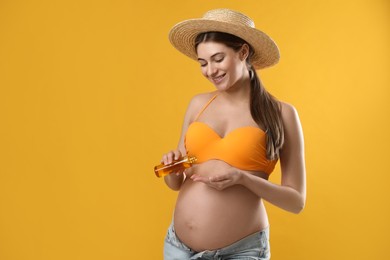 Photo of Young pregnant woman with sun protection oil on yellow background, space for text