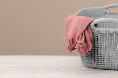 Plastic laundry basket with clothes near beige wall. Space for text