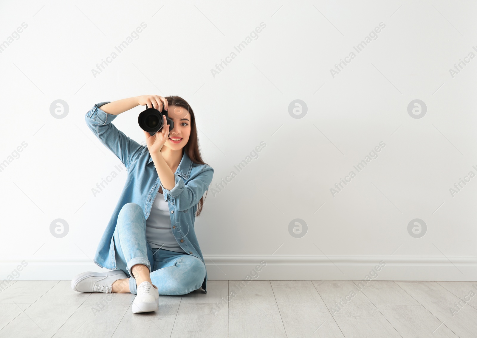 Photo of Female photographer with camera sitting on floor near wall indoors