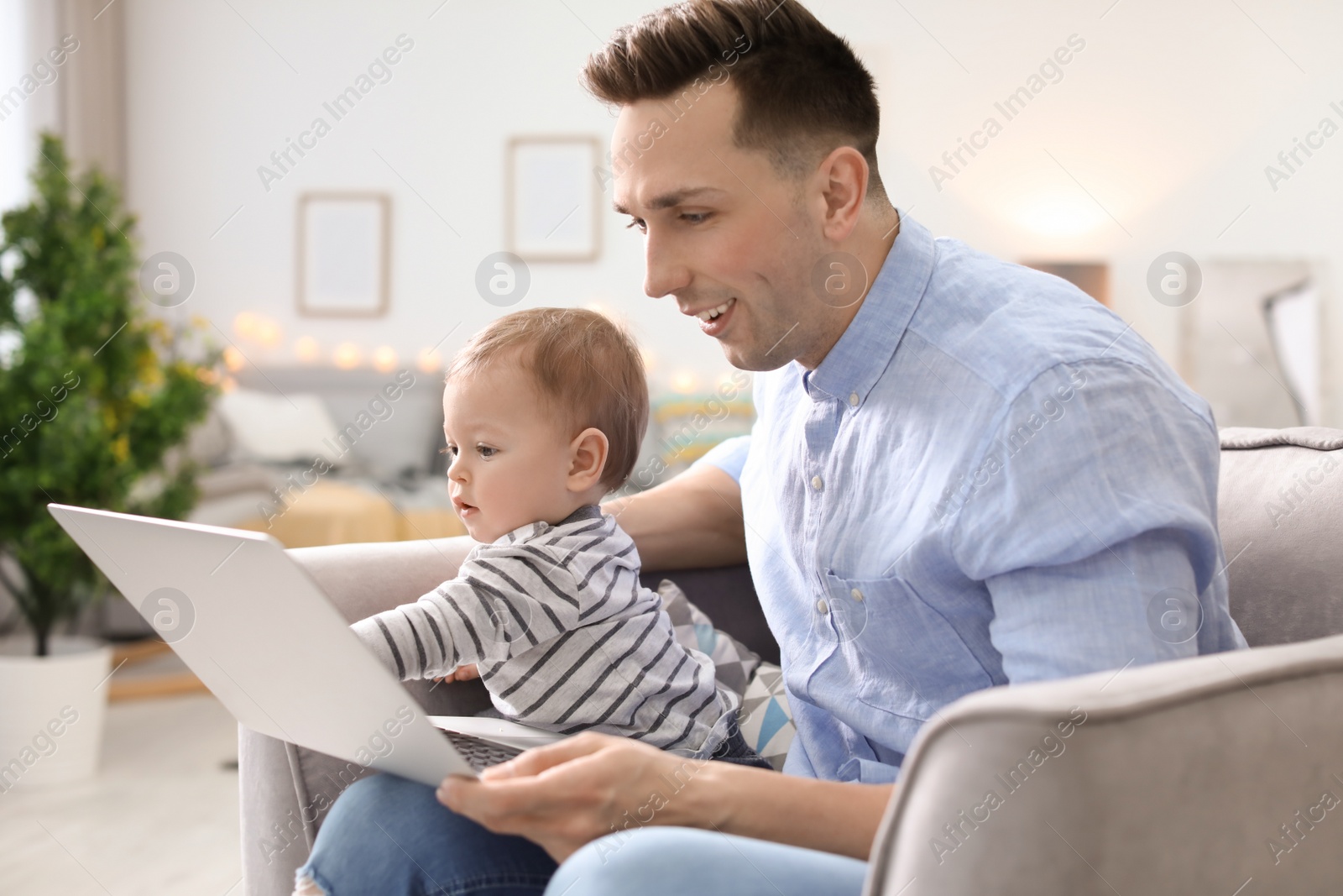 Photo of Young father with his cute little son using laptop at home