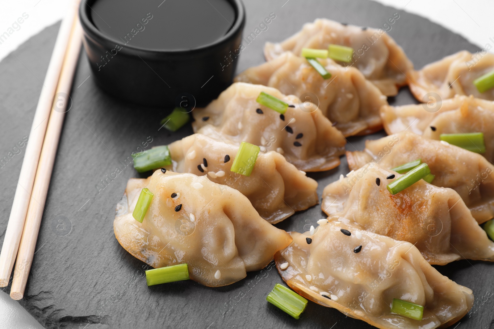 Photo of Delicious gyoza (asian dumplings) with green onions, soy sauce and chopsticks on black board, closeup