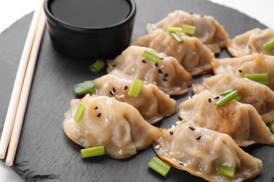 Delicious gyoza (asian dumplings) with green onions, soy sauce and chopsticks on black board, closeup