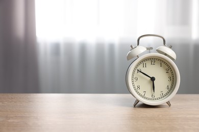 Photo of White alarm clock on wooden table indoors, space for text