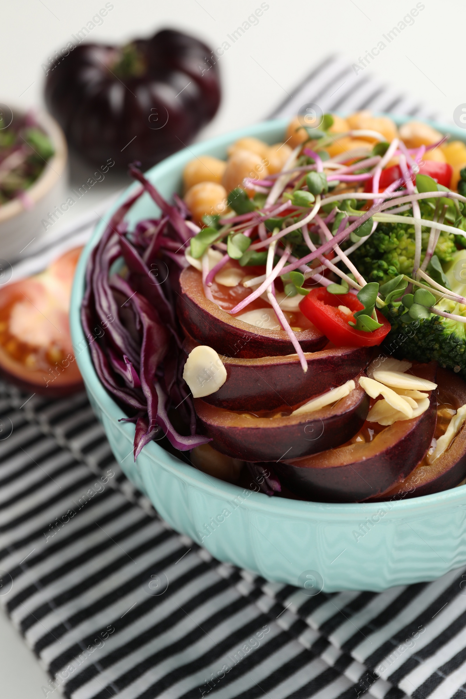 Photo of Delicious vegan bowl with broccoli, red cabbage and black tomato on grey table, closeup